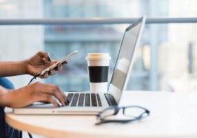 An ecommerce business owner typing on a laptop and holding a laptop with a cup of coffee